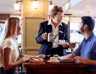 A friendly server pours coffee for a smiling couple at a cosy hotel restaurant.
