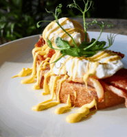 Delectable eggs benedict with bacon on toasted bread garnish with greenery, placed on table.