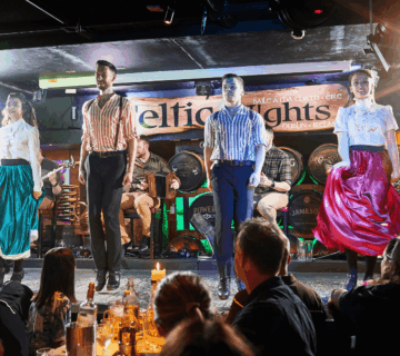 Performers in traditional Irish attire dancing on stage at a lively hotel bar.