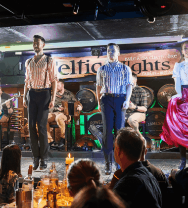 Performers in traditional Irish attire dancing on stage at a lively hotel bar.