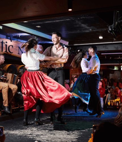 Traditional Irish dancers perform energetically on stage at a vibrant, bustling bar.
