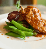Elegant chicken dish with pea pods and glazed onion at an upscale dining setting.