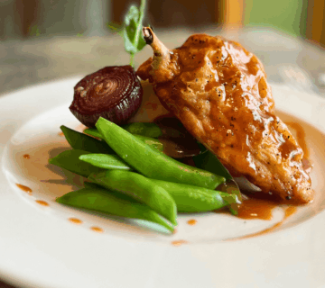Elegant chicken dish with pea pods and glazed onion at an upscale dining setting.