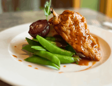 Elegant chicken dish with pea pods and glazed onion at an upscale dining setting.