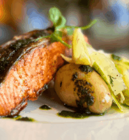 Grilled salmon and potatoes served with fresh greens in an elegant dining setting.