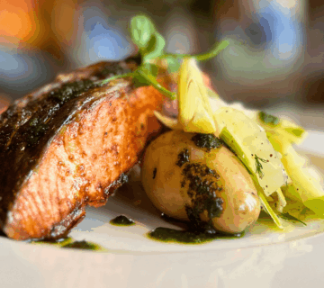 Grilled salmon and potatoes served with fresh greens in an elegant dining setting.