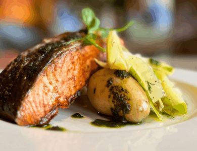 Grilled salmon and potatoes served with fresh greens in an elegant dining setting.