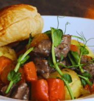 Savoury beef stew with carrots and potatoes, topped with pastry, served in a white bowl.