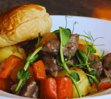 Savoury beef stew with carrots and potatoes, topped with pastry, served in a white bowl.