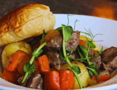 Savoury beef stew with carrots and potatoes, topped with pastry, served in a white bowl.