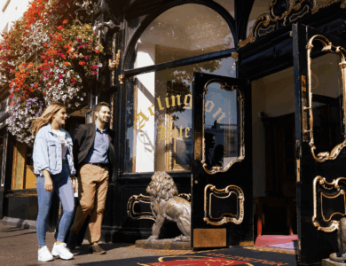 A couple walks past Arlington Hotel's ornate entrance, adorned with vibrant flowers.