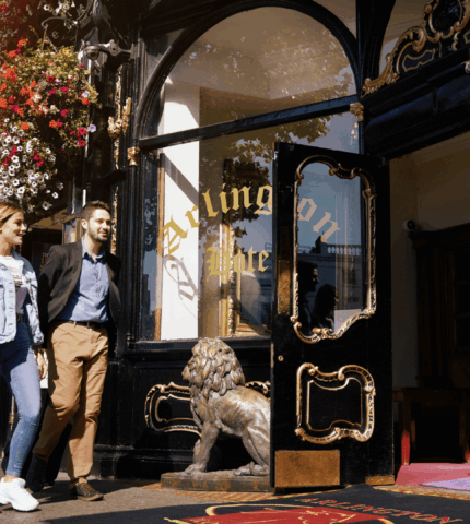 A couple walks past Arlington Hotel's ornate entrance, adorned with vibrant flowers.