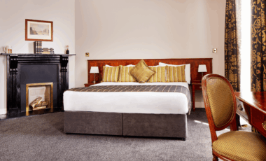 Elegant hotel room with plush bed, cosy fireplace, and tasteful decor.