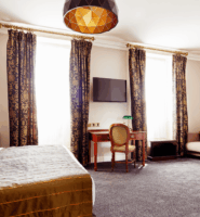 Elegant hotel room with double bed, sofa, and a window with patterned curtains.