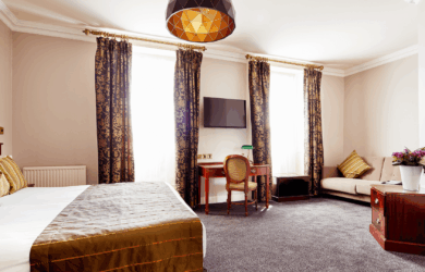 Elegant hotel room with double bed, sofa, and a window with patterned curtains.