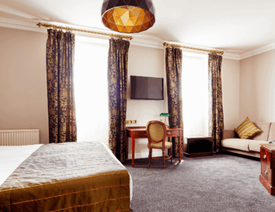 Elegant hotel room with double bed, sofa, and a window with patterned curtains.