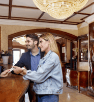 Hotel guests check in at a luxurious wooden reception desk with a friendly staff member.