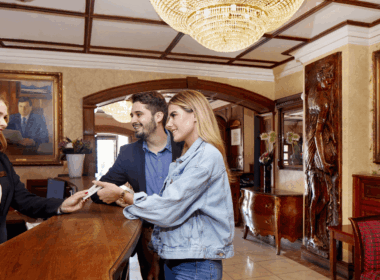 Hotel guests check in at a luxurious wooden reception desk with a friendly staff member.