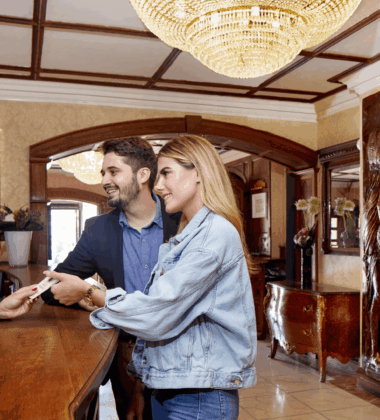Hotel guests check in at a luxurious wooden reception desk with a friendly staff member.