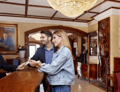 Hotel guests check in at a luxurious wooden reception desk with a friendly staff member.
