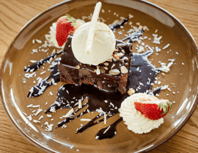 Decadent chocolate brownie with ice cream, strawberries, and whipped cream on a brown plate.
