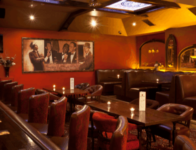 Cosy hotel bar with red seating, ambient lighting, and wall art of musicians.