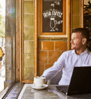 Man enjoying coffee at a cosy Dublin cafe with passersby and a bus outside.