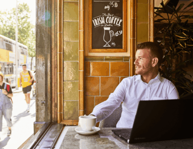 Man enjoying coffee at a cosy Dublin cafe with passersby and a bus outside.
