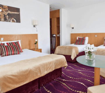 Elegant hotel room with a king bed, two single beds, and stylish decor in warm tones.