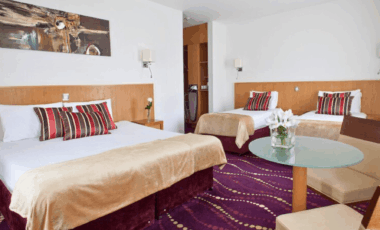 Elegant hotel room with a king bed, two single beds, and stylish decor in warm tones.