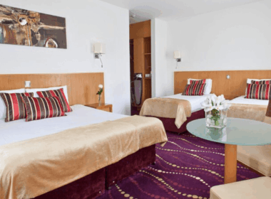 Elegant hotel room with a king bed, two single beds, and stylish decor in warm tones.