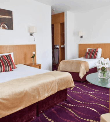 Elegant hotel room with a king bed, two single beds, and stylish decor in warm tones.