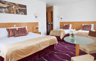Elegant hotel room with a king bed, two single beds, and stylish decor in warm tones.