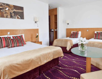 Elegant hotel room with a king bed, two single beds, and stylish decor in warm tones.