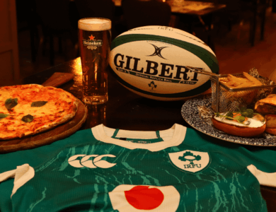 Delicious pizza, burger, and beer with a rugby jersey at a cosy bar setting.