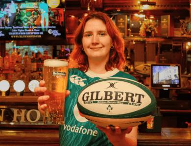 Person holding a pint and rugby ball in a warm, inviting bar atmosphere.