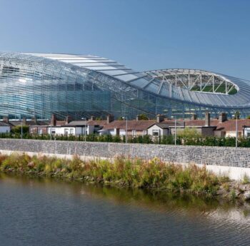 Modern stadium near riverside houses in Dublin, sunny day scene.
