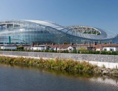 Modern stadium near riverside houses in Dublin, sunny day scene.