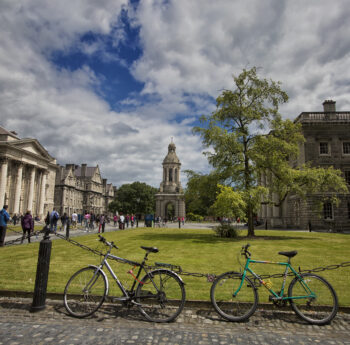 Scenic view of Trinity College Dublin with visitors strolling and bicycles parked nearby.
