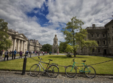 Scenic view of Trinity College Dublin with visitors strolling and bicycles parked nearby.