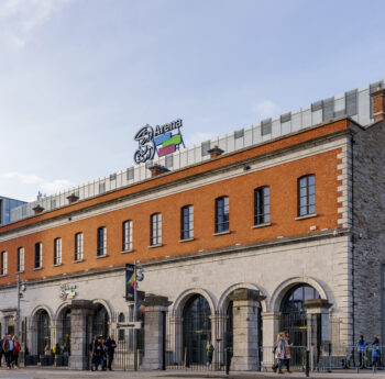 People strolling outside a historic building near 3Arena in Dublin.