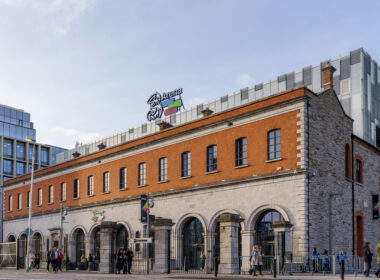 People strolling outside a historic building near 3Arena in Dublin.