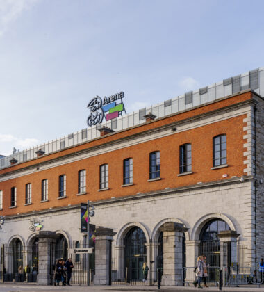 People strolling outside a historic building near 3Arena in Dublin.