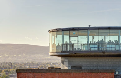 Modern glass rooftop bar with guests enjoying panoramic views over Dublin's scenic landscape.