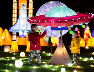 Two children enjoying colourful lanterns at night with a space theme.