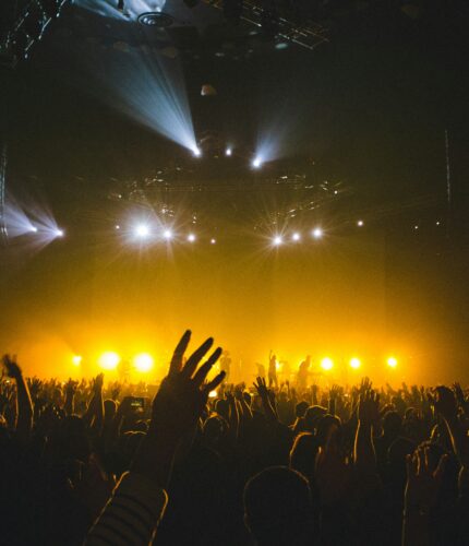 Excited crowd enjoying a live music concert with vibrant yellow stage lighting.