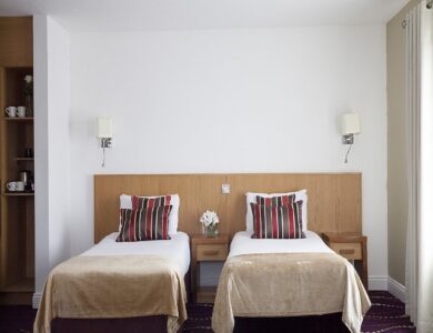Twin beds with striped cushions, modern decor, and soft lighting in a cosy hotel room.