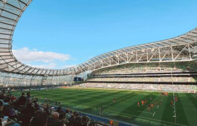 Spacious stadium with attendees watching a lively rugby match under a clear blue sky.