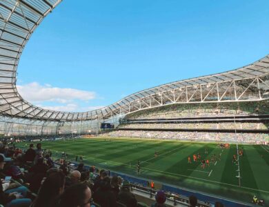 Spacious stadium with attendees watching a lively rugby match under a clear blue sky.