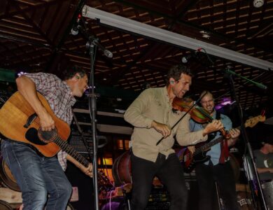 Musicians energetically perform with guitar, violin, and bass at a lively hotel bar.